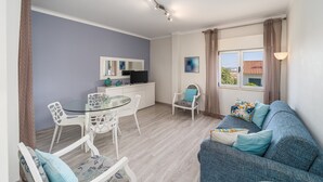 Un salon moderne avec une table à manger en verre, des chaises blanches, un canapé bleu et un téléviseur.