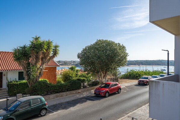 Une vue de rue avec des voitures garées, un grand arbre et un bâtiment avec un toit rouge.