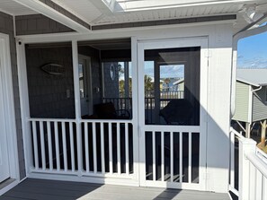 A covered porch with a white railing, a door, and a view of a residential area.