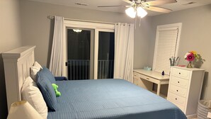 Quarto com cama, escrivaninha, cômoda, abajur e ventilador de teto.