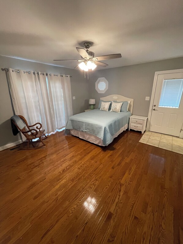 A bedroom with a bed, a rocking chair, a ceiling fan, and a door with a window.