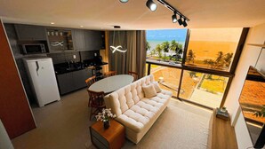 A modern kitchen with a dining area and a sofa facing a large window with a beach view. - Flat FM20 Cabo Branco Deluxe - By Almare (João Pessoa)