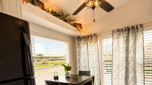 A kitchen with a refrigerator, a dining table with chairs, a ceiling fan, and windows with curtains. - Peaceful Pondside Stay (Archie)