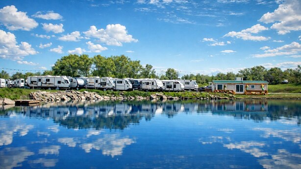 A row of RVs parked by a calm lake with a small house in the background. - Peaceful Pondside Stay (Archie)
