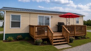 A mobile home with a deck, a grill, and a red umbrella. - Peaceful Pondside Stay (Archie)