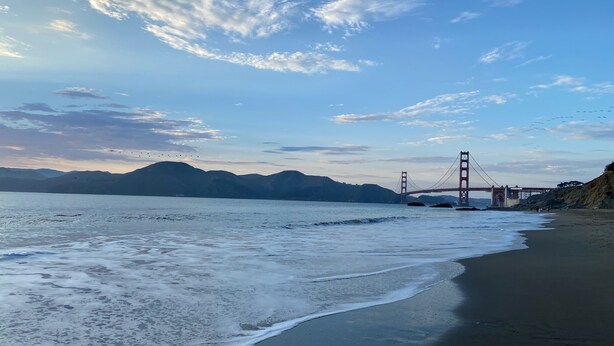 A beach with waves, a distant bridge, and mountains. - Da Hotel OCt (North Vancouver)