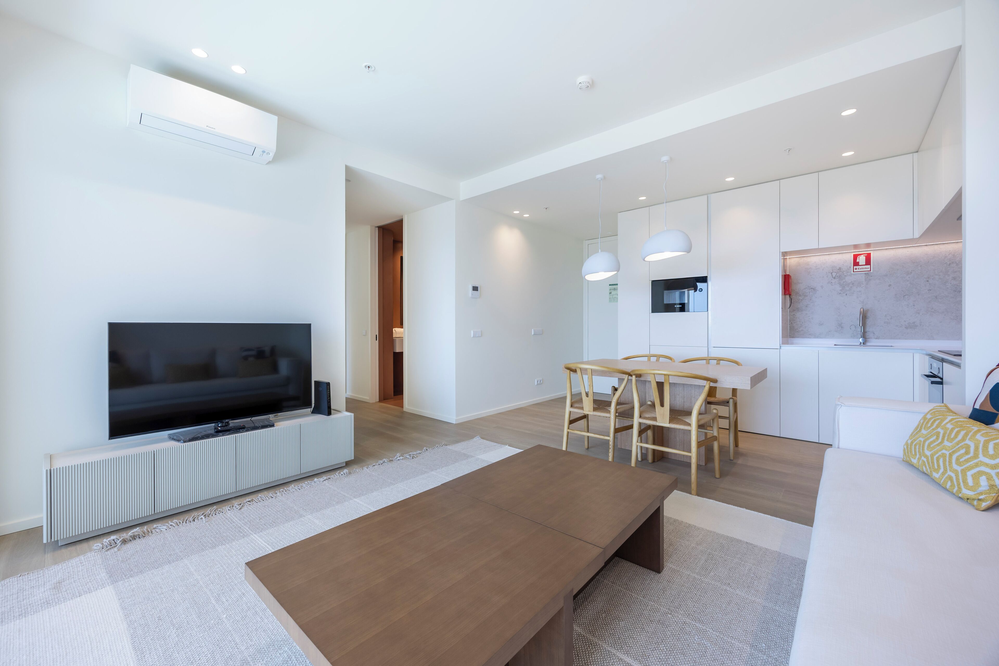 Una sala de estar moderna con una televisión de pantalla plana, una mesa de centro de madera y un comedor con una mesa blanca y sillas de madera.