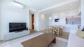 Una sala de estar moderna con una televisión de pantalla plana, una mesa de centro de madera y un comedor con una mesa blanca y sillas de madera.