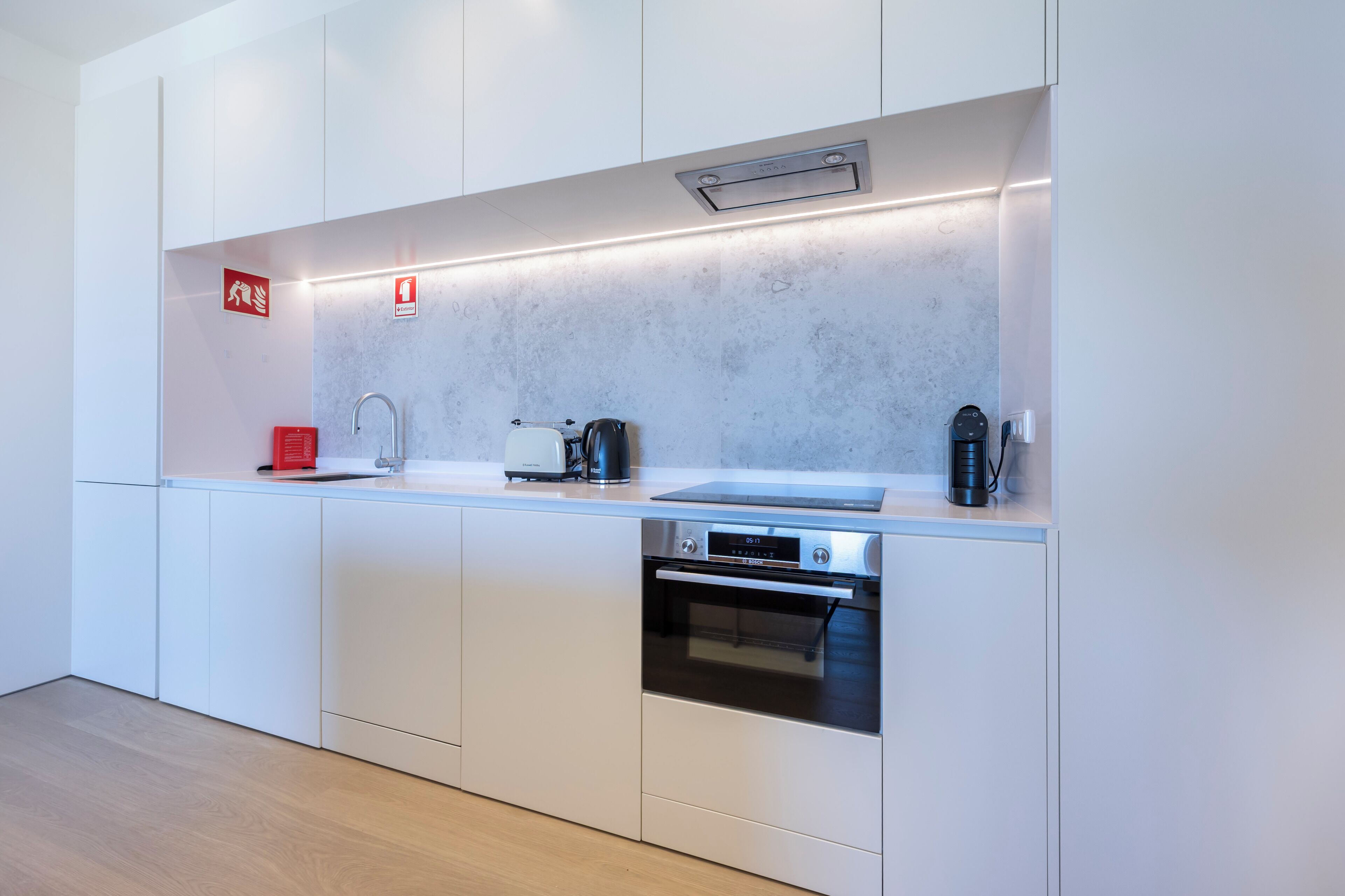 A modern kitchen with white cabinetry, a stainless steel sink, a Bosch coffee machine, and a built-in oven.