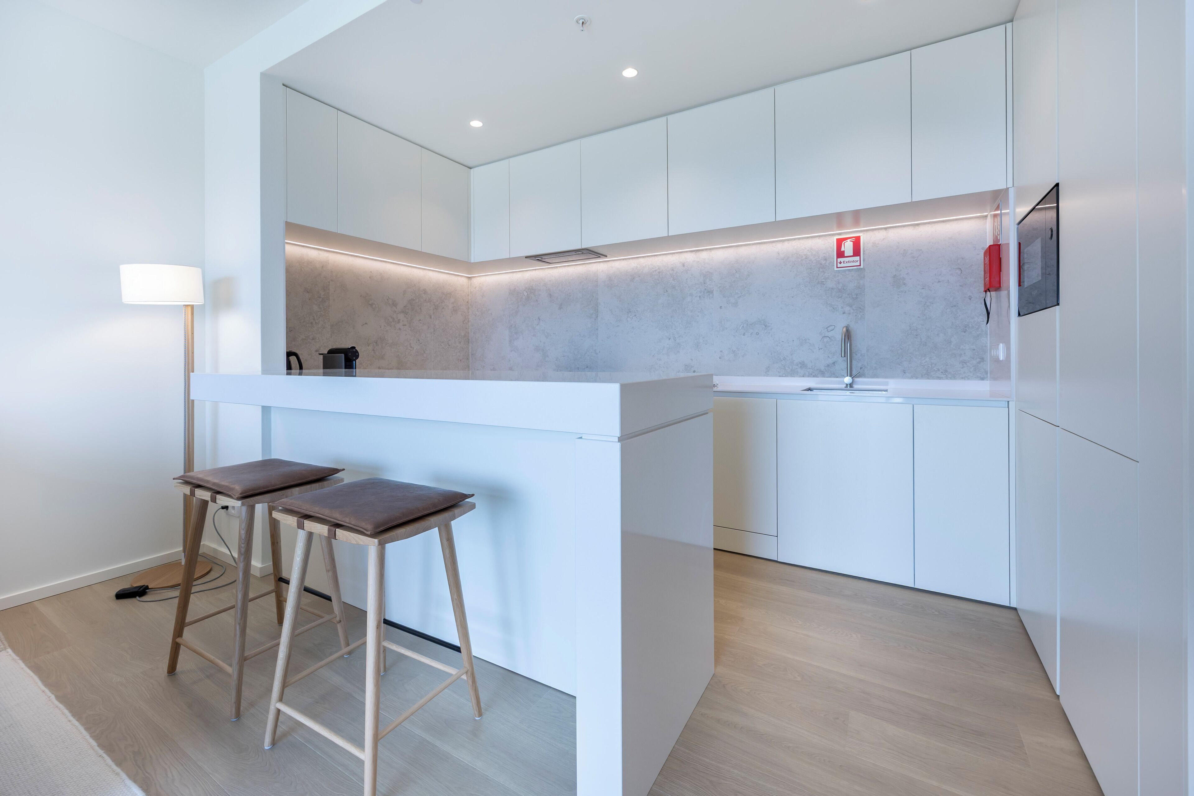 A modern kitchen with white cabinetry, a built-in stove, and a small bar area with stools.