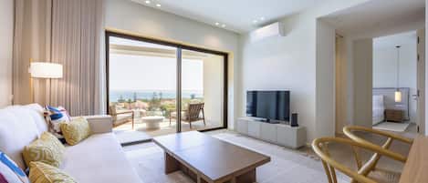 A modern hotel room with a sofa, a wooden coffee table, a TV, and a balcony with a view.