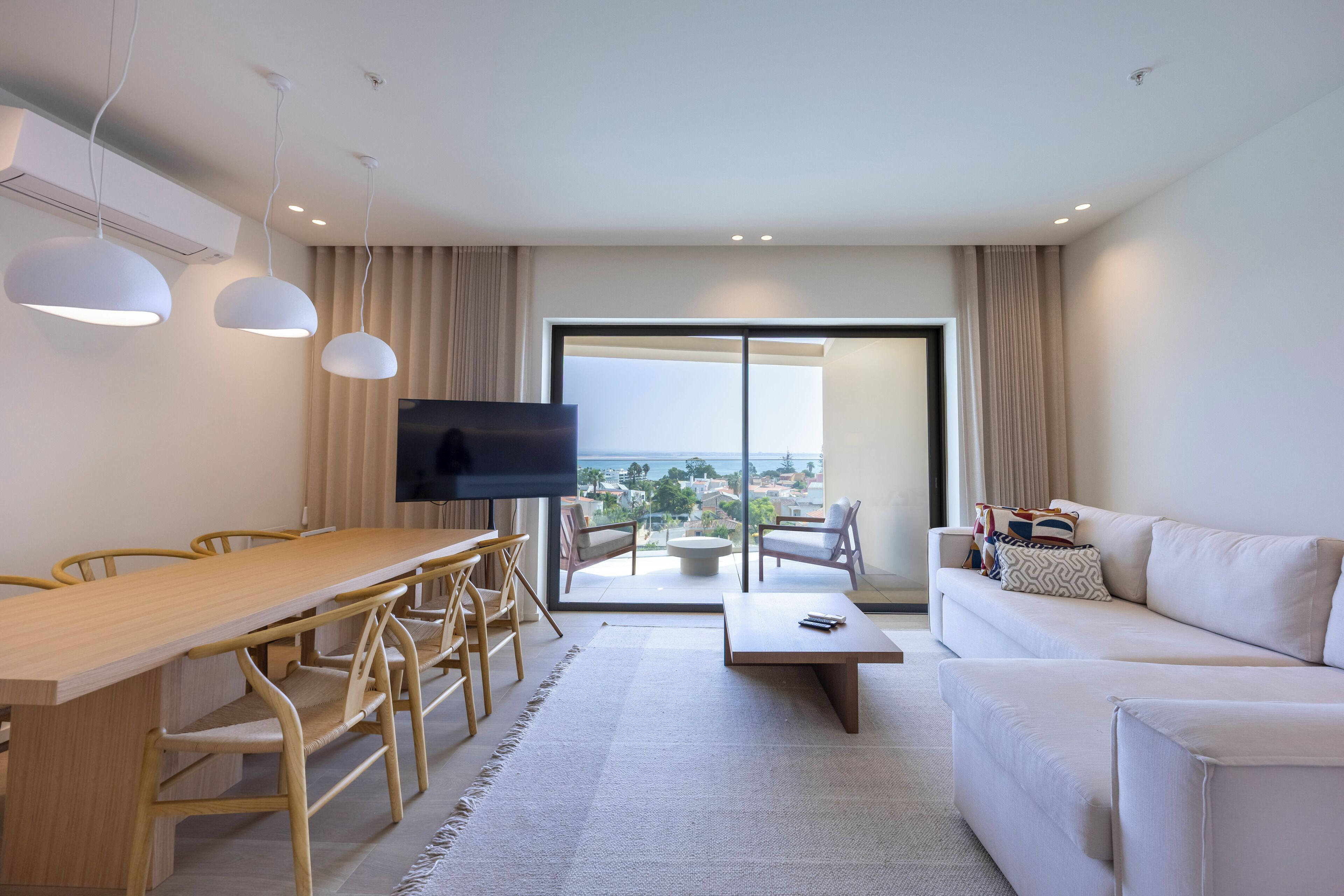 Een moderne woonkamer met een houten eettafel, een witte bank en een flatscreen televisie.