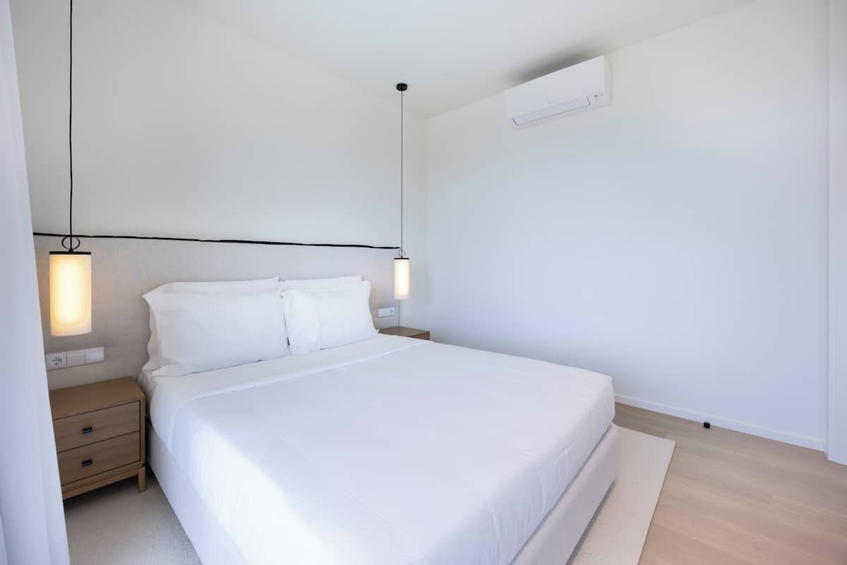 A minimalist bedroom with a large bed, bedside tables, and pendant lighting.