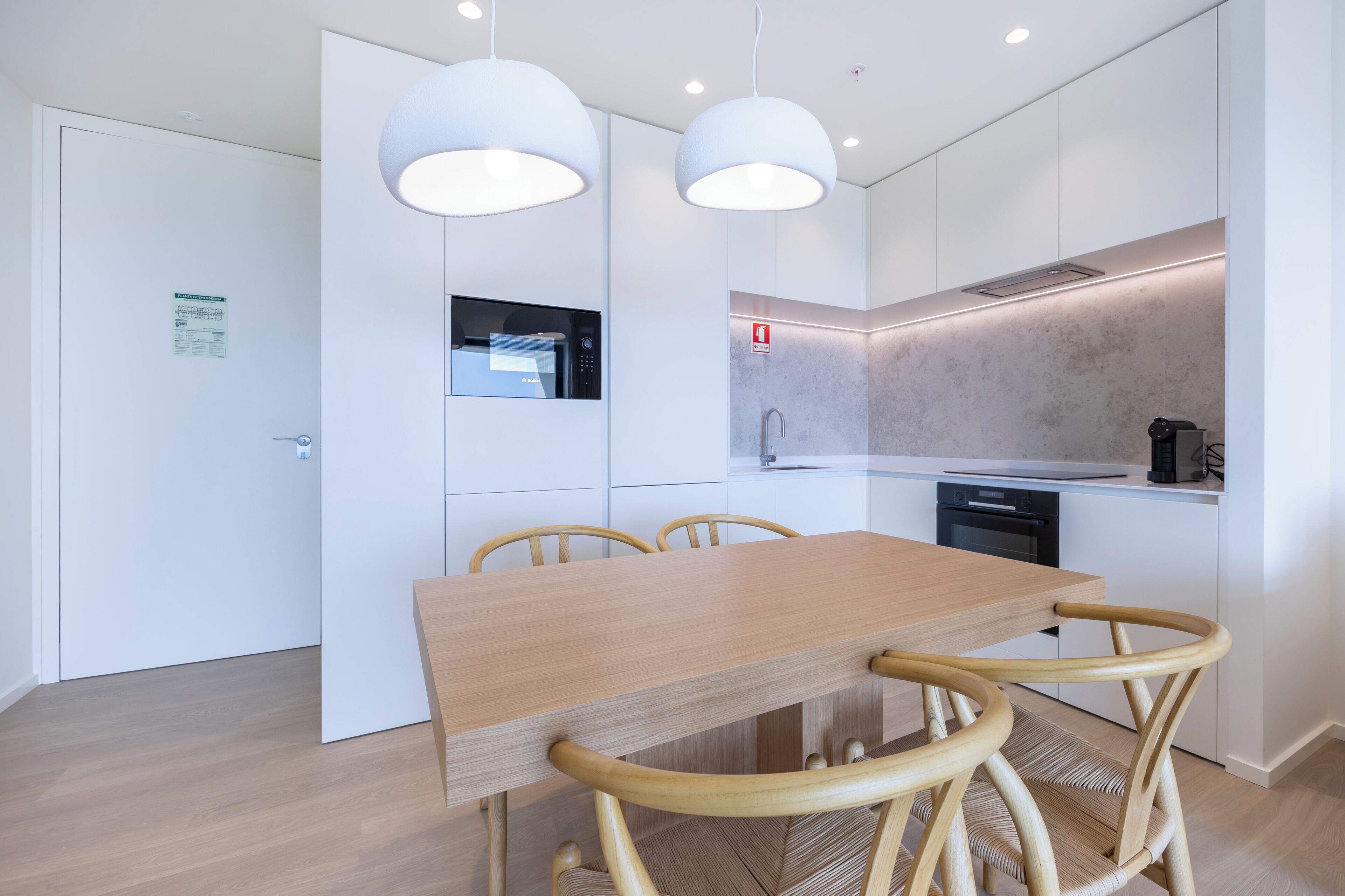 A modern kitchen with white cabinets, a wooden dining table, and two pendant lights.