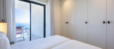 Un dormitorio con una cama grande, un ventanal corredero que da a un balcón y un armario blanco.