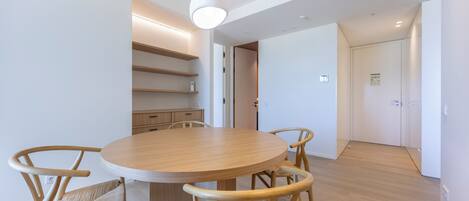 A modern dining area with a round wooden table and four chairs, a built-in shelf unit, and a ceiling-mounted light fixture.