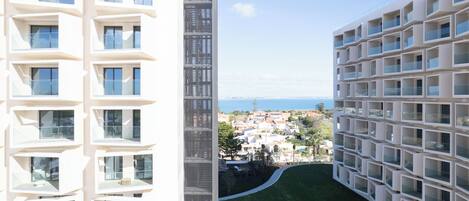 A modern building with multiple balconies, a central vertical structure, and a view of a coastal town.