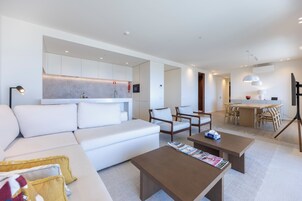 A modern living room with a white sofa, wooden chairs, a coffee table, and a dining area with a wooden table and chairs.