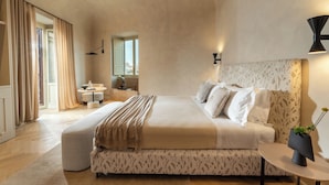 A spacious bedroom with a large bed, a bedside table, a window with curtains, and a view of the outdoors. - Palazzo Balsamo  (Palermo)