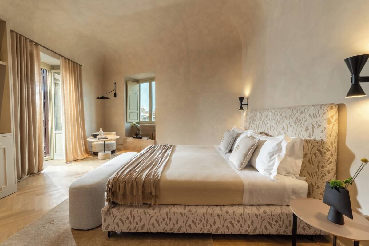 Une chambre spacieuse avec un grand lit, une table de chevet, une fenêtre avec des rideaux et une vue sur l’extérieur.