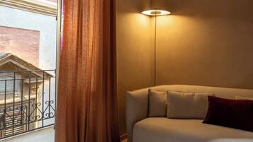 A room with a sofa, a lamp, a window with curtains, and a view of a building outside.