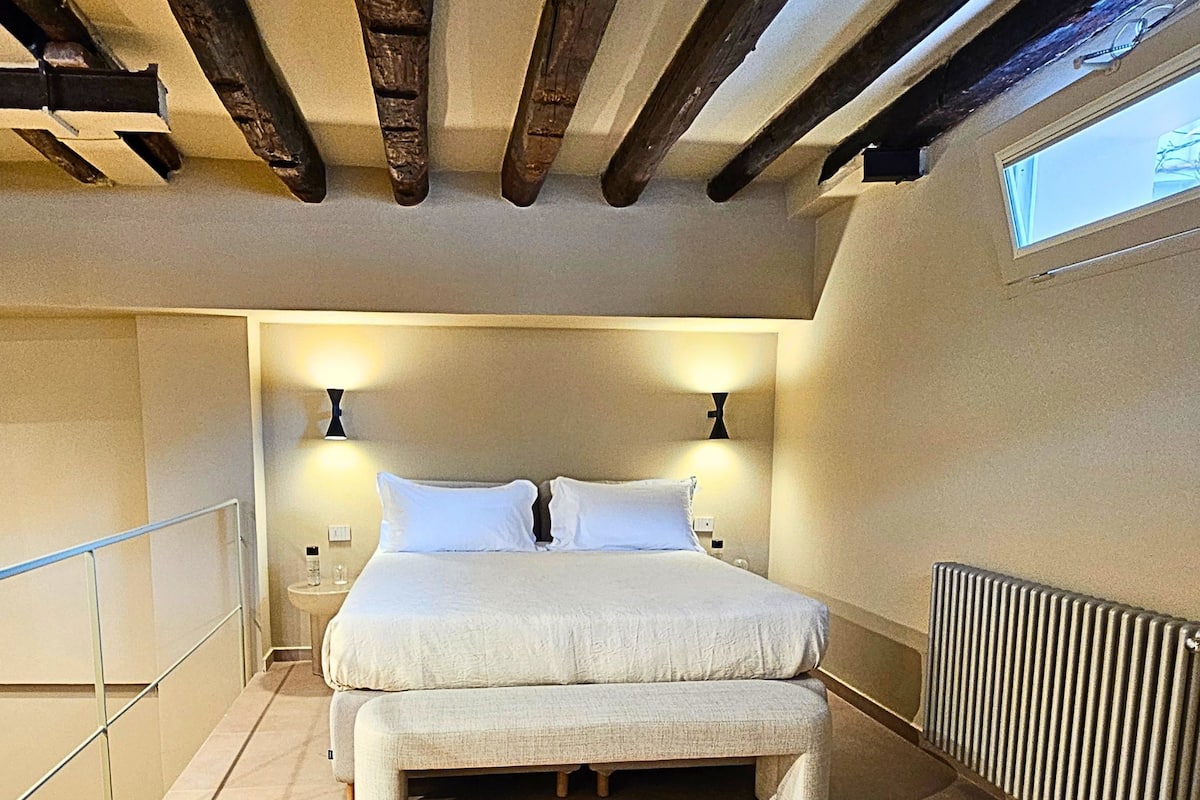 Une chambre avec un grand lit, des poutres en bois, un radiateur et une fenêtre.