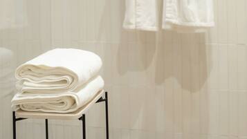 A bathroom with two white robes hanging on hooks and a stack of folded white towels on a small table.