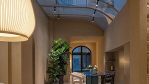 A spacious living area with a high ceiling, a large potted plant, a dining table with chairs, and a view through a glass balcony. - Palazzo Balsamo  (Palermo)