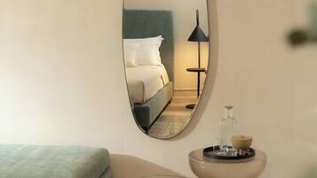 A modern hotel room with a large oval mirror reflecting a neatly made bed, a bedside lamp, and a small table with a tray of cookies.