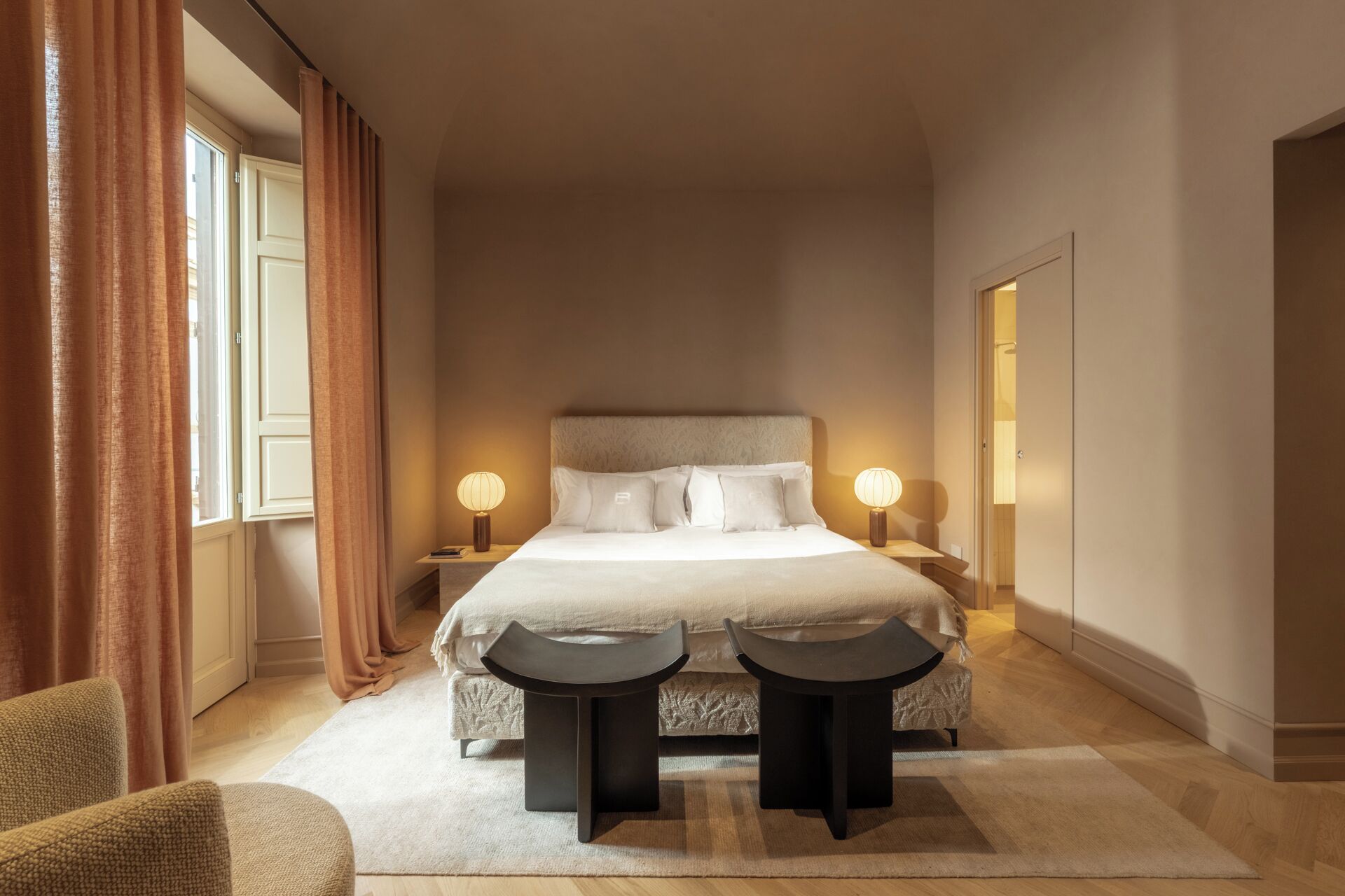 A hotel room with a large bed, two bedside tables with lamps, a small round table, and a chair.