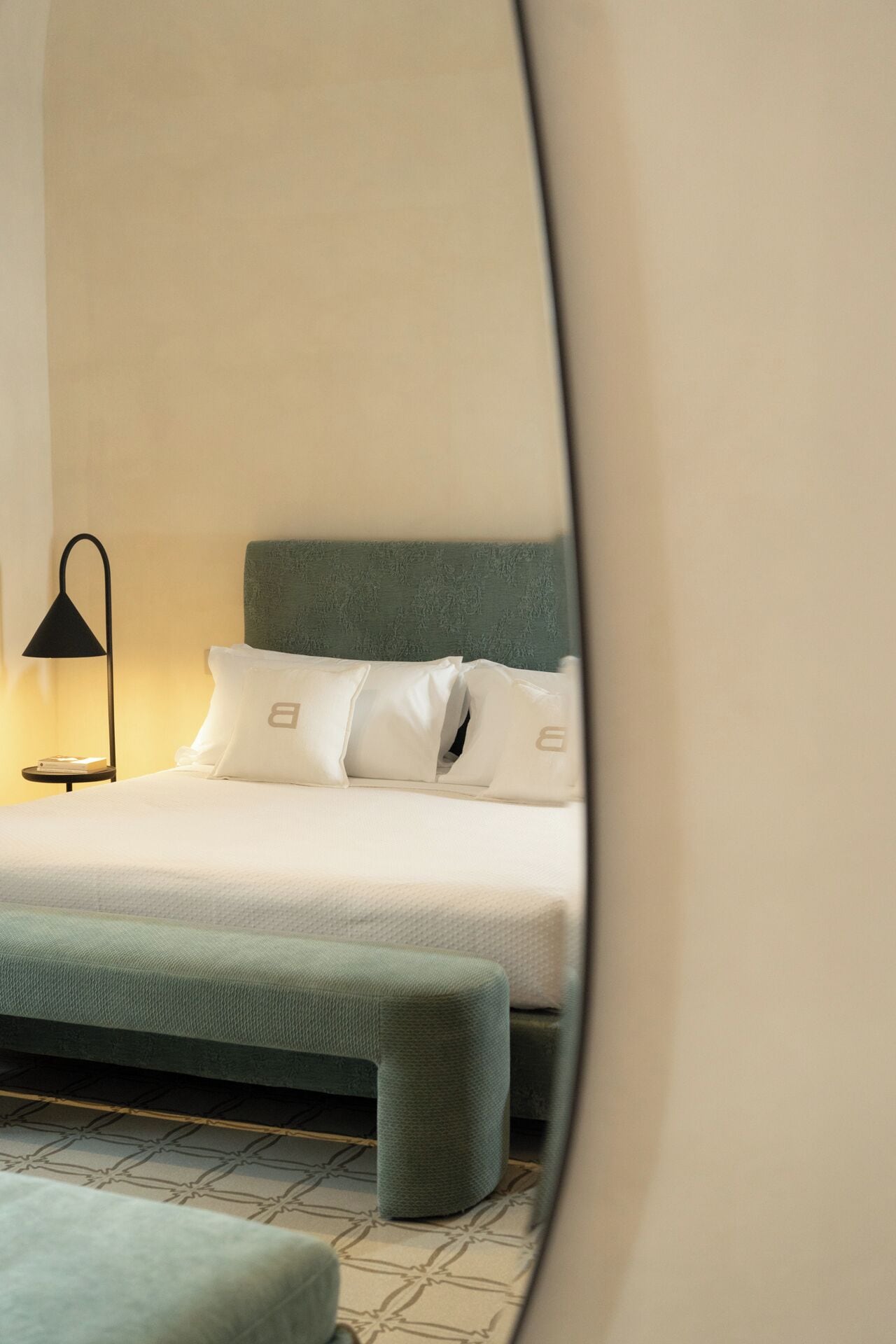 Una cama bien hecha con cabecera verde, almohadas blancas y una lámpara de noche.