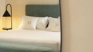 Una cama bien hecha con cabecera verde, almohadas blancas y una lámpara de noche.