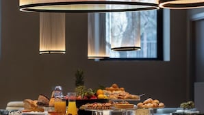 A breakfast buffet with various pastries and fruits, set in a room with large windows and modern pendant lights. - Palazzo Balsamo  (Palermo)