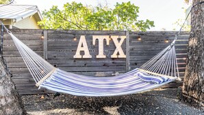 A hammock tied between two trees with a wooden fence in the background displaying the letters "ATX". - 5BR Oasis - Pool + Hot Tub + Games - Walk to Fun! (Austin)