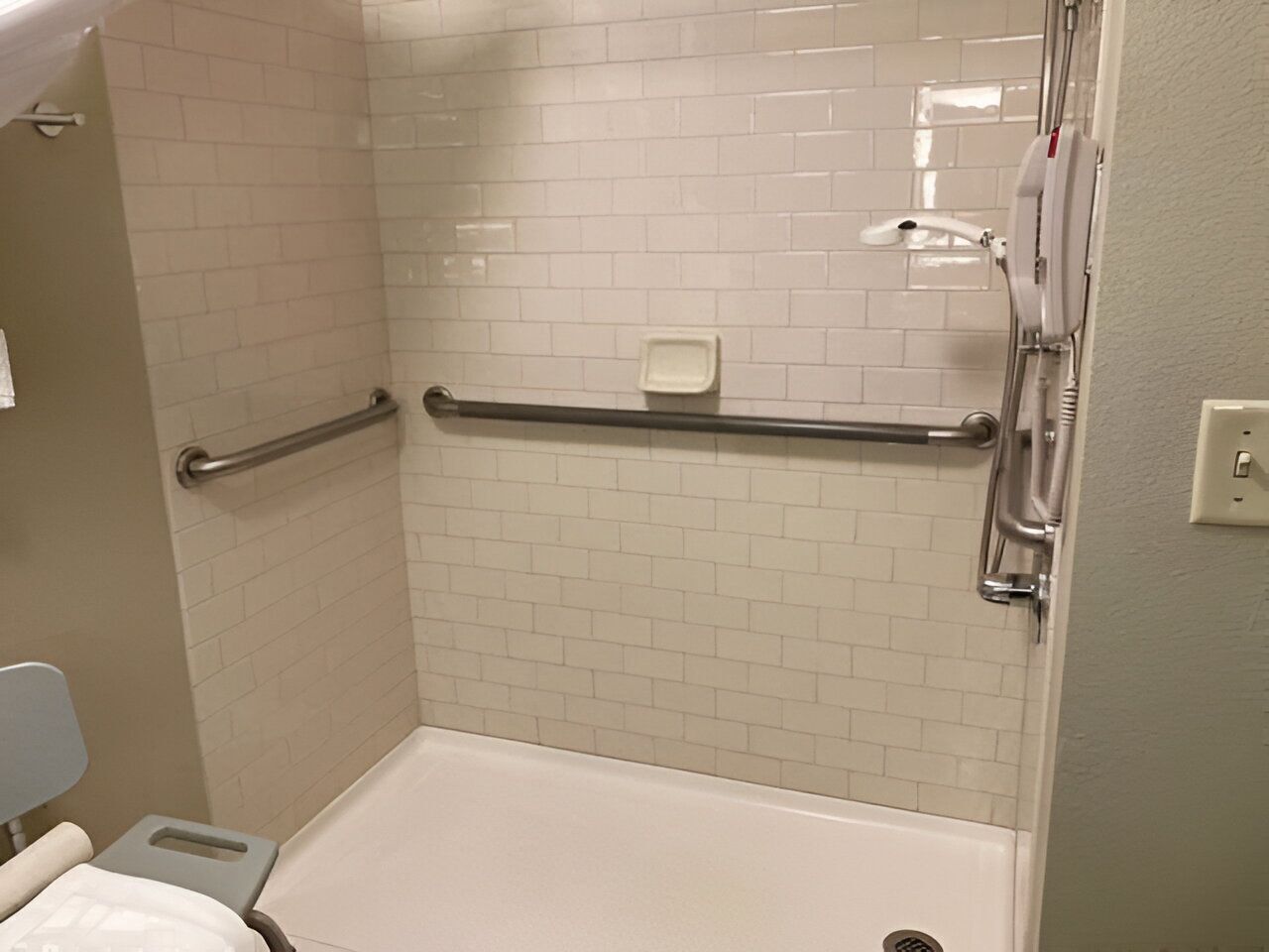 A shower area with white tiled walls, a grab bar, and a handheld showerhead.