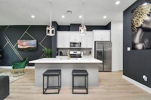 A modern kitchen with a central island, white cabinets, stainless steel appliances, and pendant lighting.