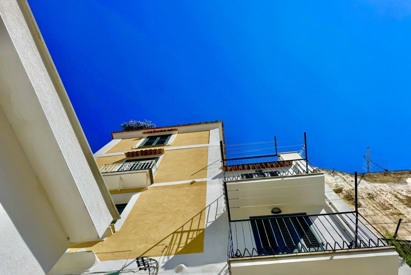 Un edificio de varios pisos con balcones, cielo azul despejado y una colina al fondo.