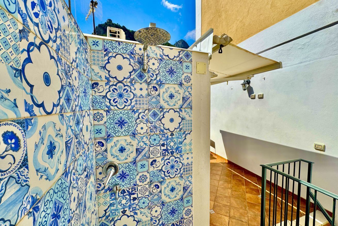 Un pasillo con baldosas blancas y azules estampadas, una barandilla de metal y una pared blanca con una puerta.