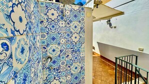 A corridor with blue and white patterned tiles, a metal railing, and a white wall with a door.