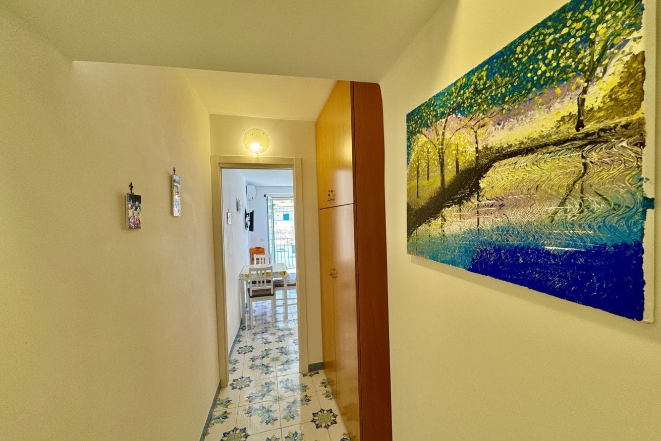 Un pasillo con piso de baldosas, una puerta de madera y un cuadro en la pared.