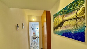 A hallway with a tiled floor, a wooden door, and a painting on the wall.