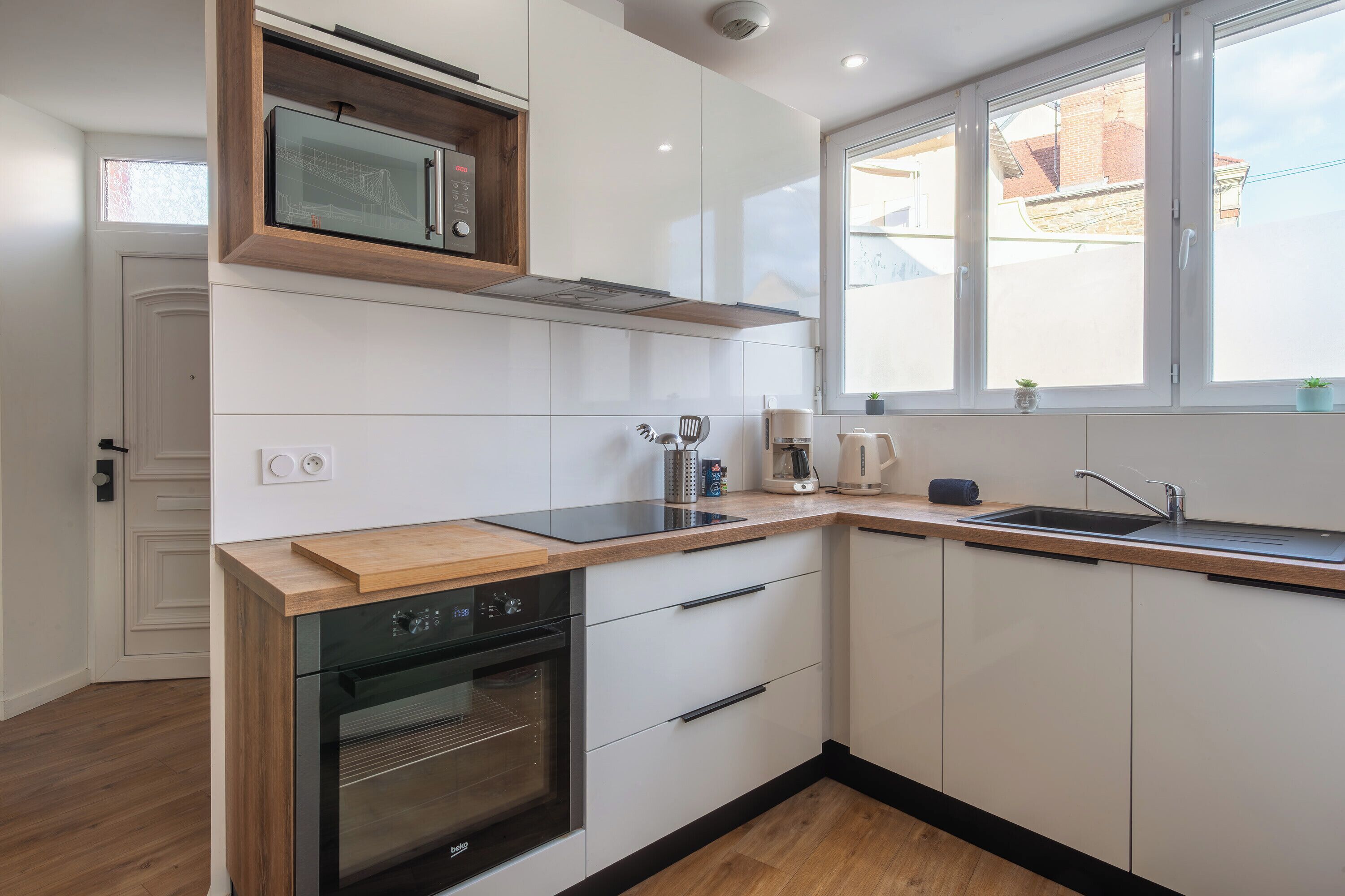 A modern kitchen with white cabinets, a wooden countertop, a built-in oven, a microwave, a sink, and a window with a view of the outside.