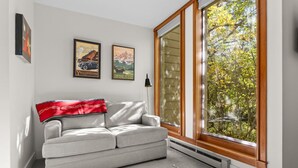 Een moderne woonkamer met een grijze bank, een rode plaid en twee ingelijste posters van Yellowstone en Grand Teton National Parks.