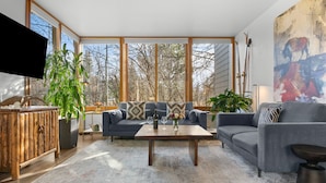 Een ruime woonkamer met een groot raam, een houten kast, een zithoek en een salontafel.