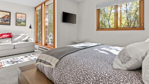Een moderne slaapkamer met een groot bed, een bank, een televisie en een raam met uitzicht op bomen.