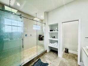 Ein modernes Badezimmer mit einer gläsernen Duschkabine, einem begehbaren Kleiderschrank mit Regalen und einer sichtbaren Mülleimer.