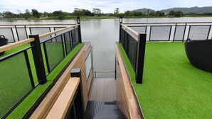 A view from a deck with a wooden railing, a small staircase, and a grassy area leading to a body of water. - Blueskyraft Resort (Kanchanaburi)