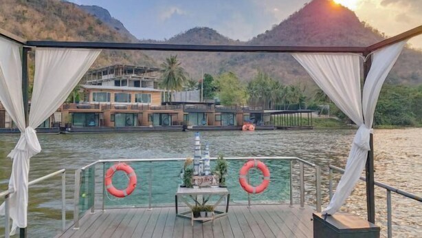 A covered outdoor area with a view of a river and mountains, featuring a table with plants and a life ring. - Blueskyraft Resort (Kanchanaburi)