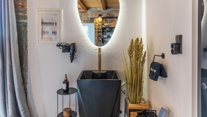 Ein modernes Badezimmer mit einem einzigartigen spiegelartigen Herz, einem schwarzen Waschbecken und einem Holzkabinet.