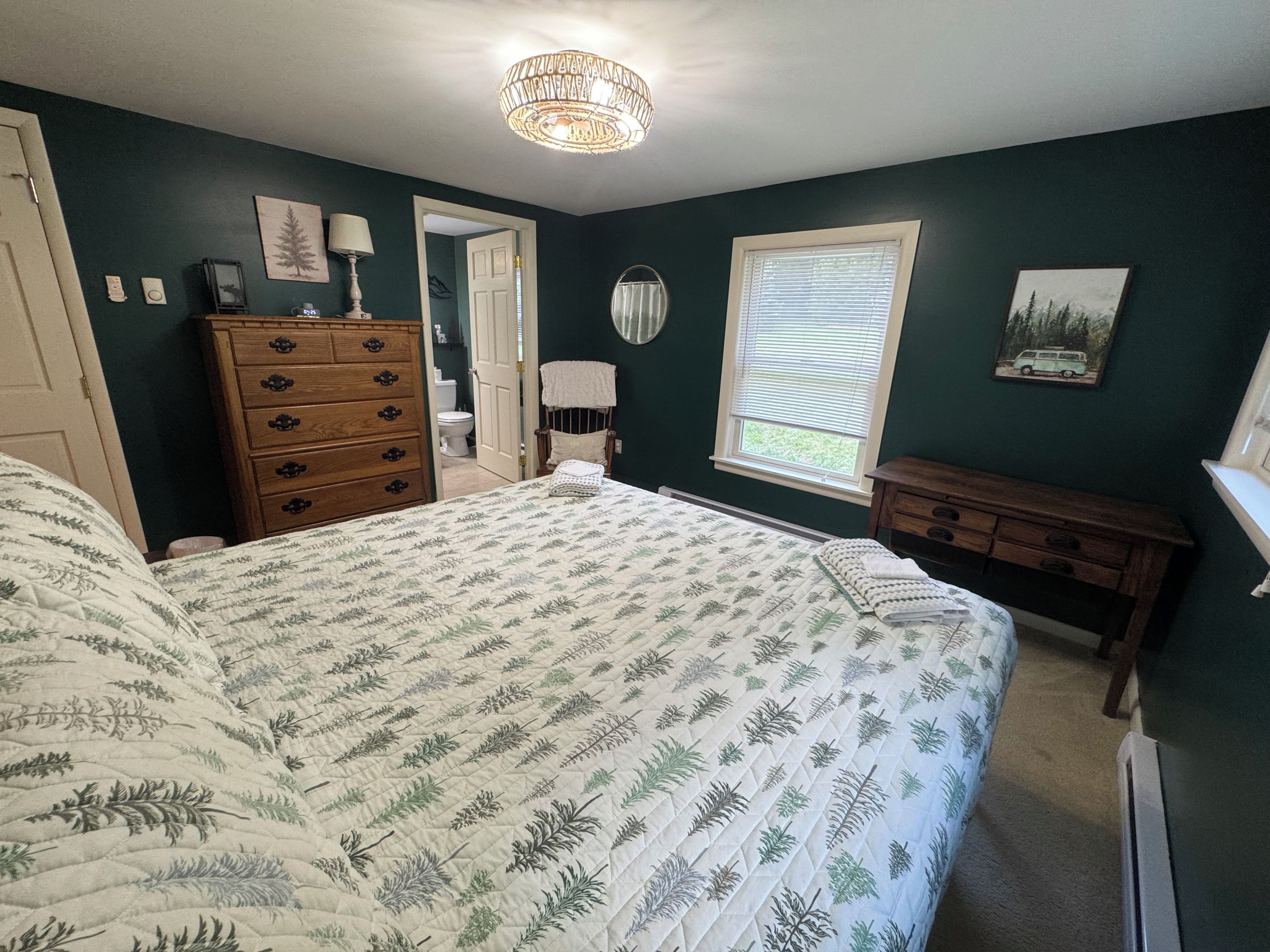 A bedroom with a large bed, dresser, and a window with blinds.